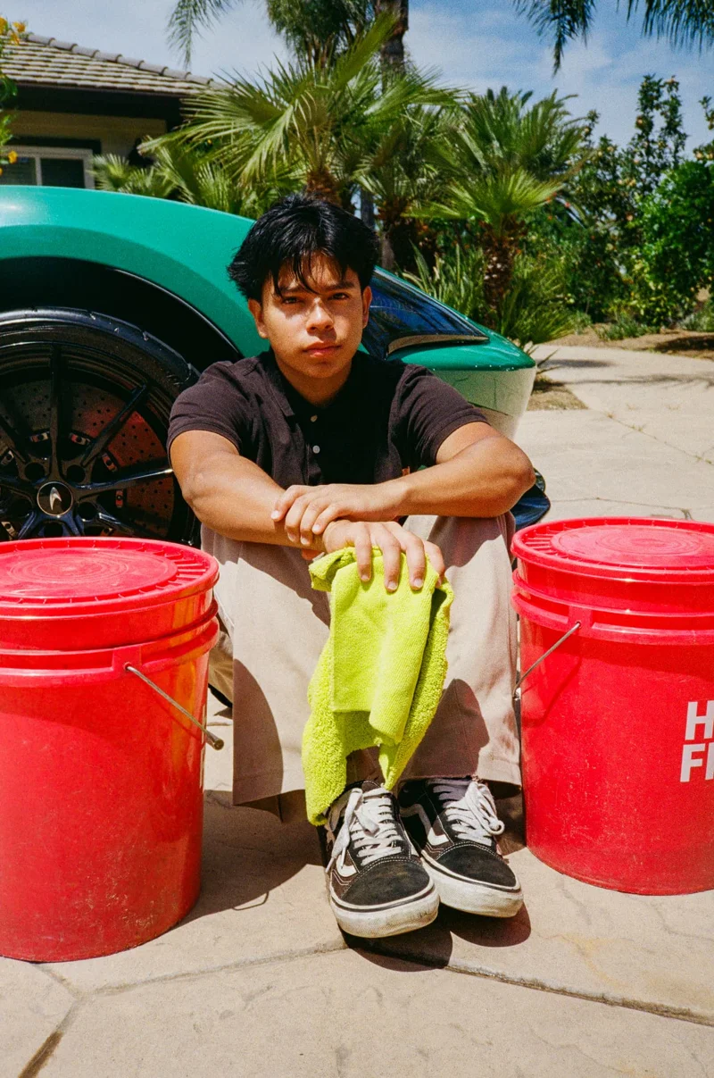 George Crabbe, owner of CCW Detailing, sitting beside a green sports car with detailing buckets and a microfiber towel