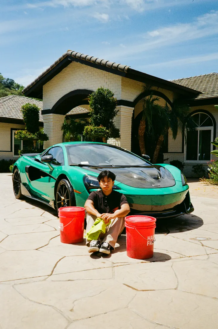 Detailer with wash buckets in front of a teal McLaren